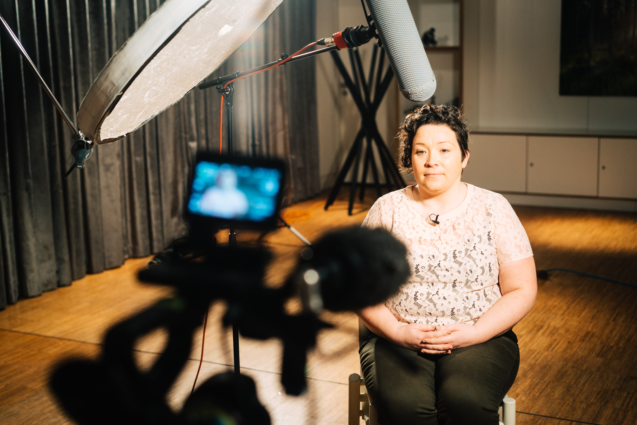 Woman sitting in front of camera in studio interview setup.