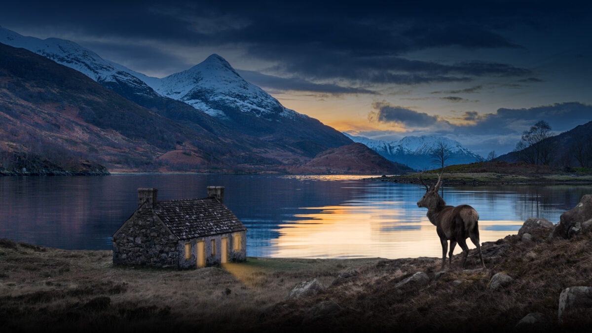 Image of a croft and a stag in front of a lake, as the sun sets over snowy hills.