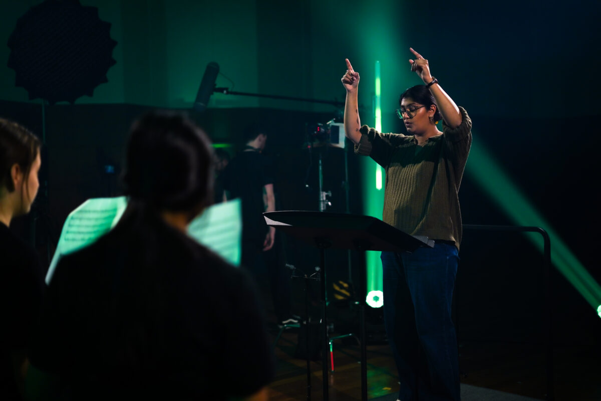 Conductor facing young people in the studio with green lights